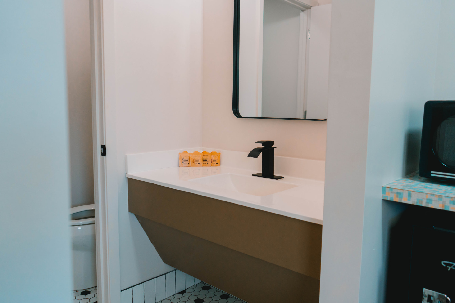 Guest bathroom vanity with a black faucet, framed mirror, and hexagon tile floor